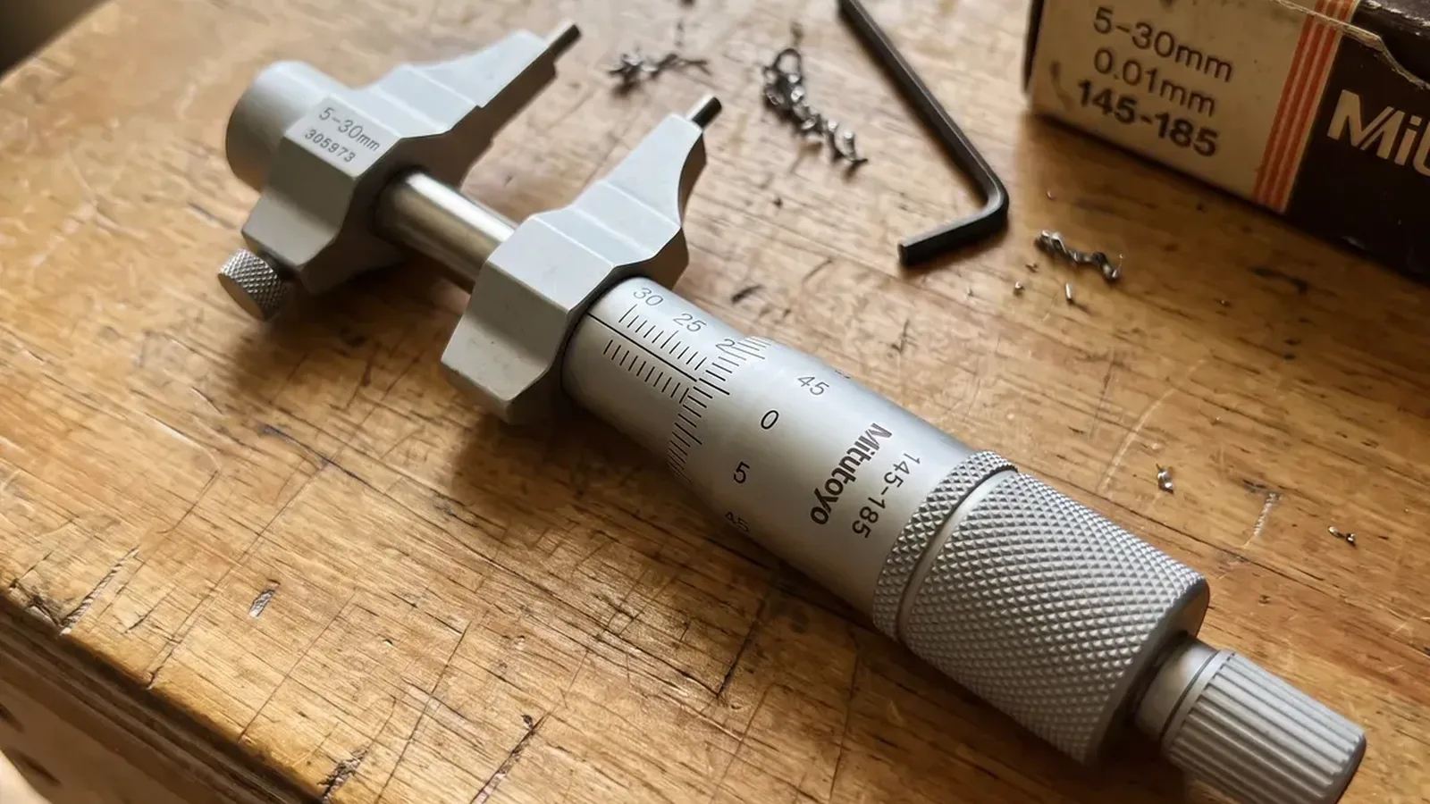 A micrometer gauge on a wooden workbench with small metal parts nearby.